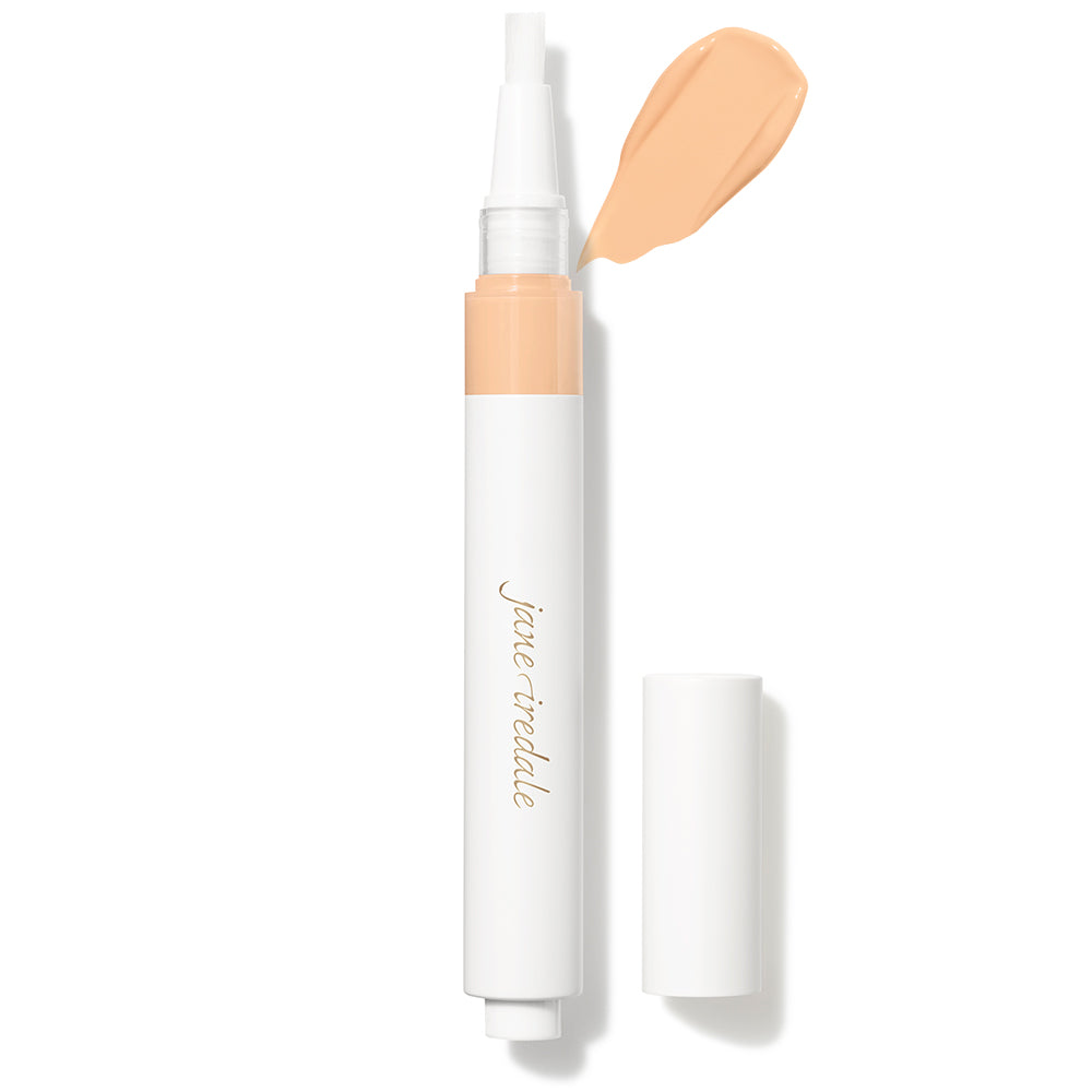 jane iredale Concealer-Stift im weiß-goldenen Gehäuse mit abgenommener Kappe. Ein hell-pfirsich-beiger Creme-Swatch direkt über dem sichtbaren Pinsel-Applikator zeigt die Produktfarbe und -konsistenz auf weißem Hintergrund.