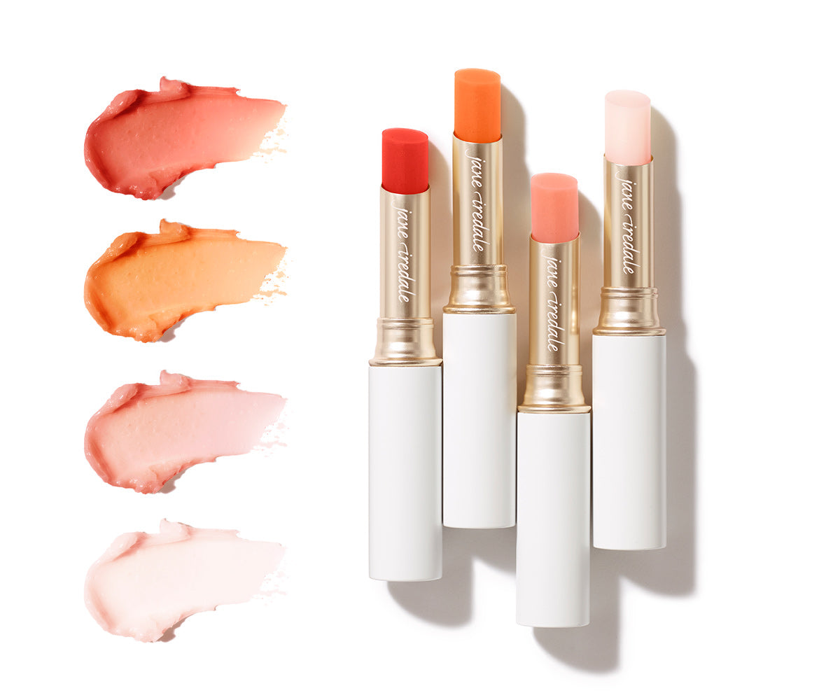 Vier geöffnete Jane Iredale Just Kissed Lip & Cheek Stains in Gold-Weiß-Optik neben farblich passenden Cremetextur-Swatches in Rot-, Orange- und Rosétönen auf weißem Hintergrund