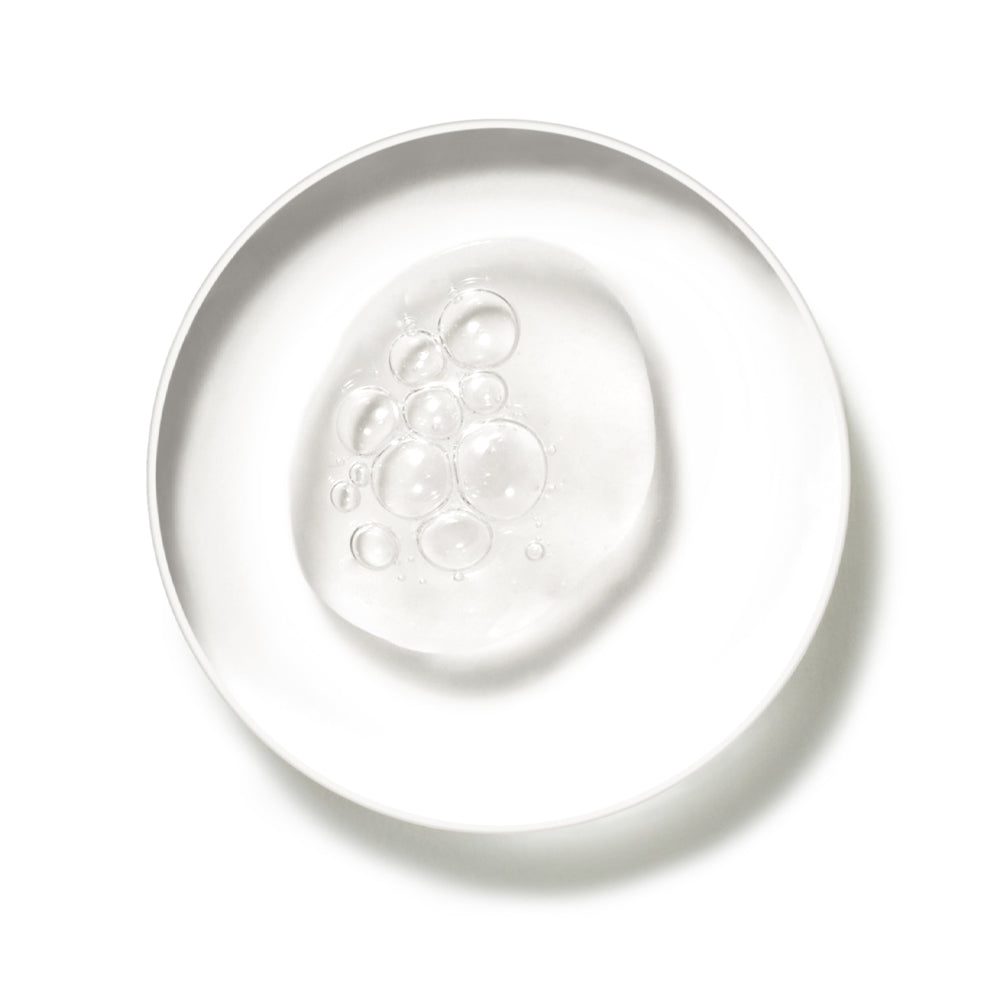 Draufsicht auf eine kleine weiße Schale mit einem transparenten Gelée-Swatch, der Luftblasen enthält, auf weißem Hintergrund.