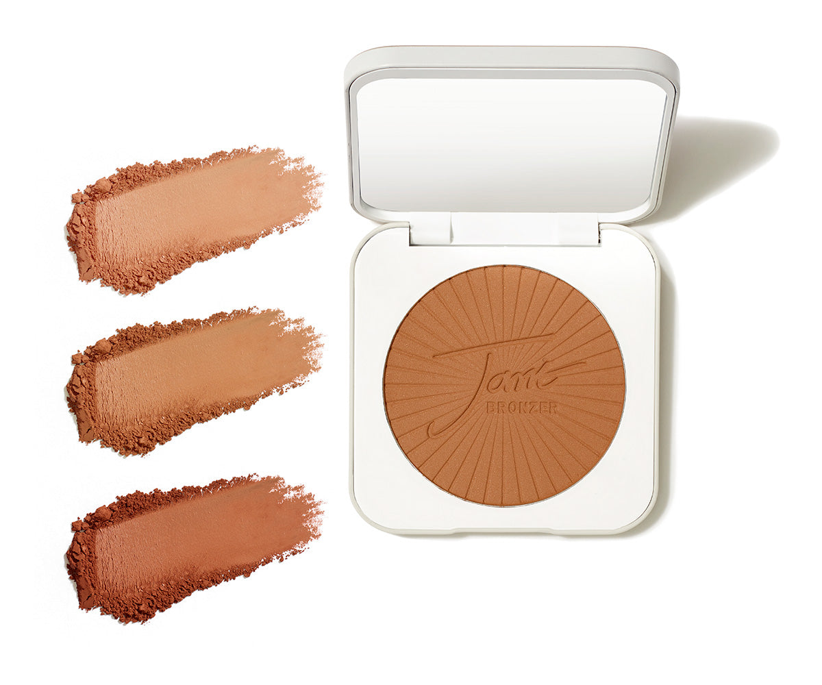 Eine geöffnete, weiße Jane Iredale Bronzer-Puderdose mit Spiegel und eingeprägtem Logo im Puder; links daneben drei Puder-Swatches in verschiedenen Braunabstufungen von Hell bis Dunkel auf weißem Grund.